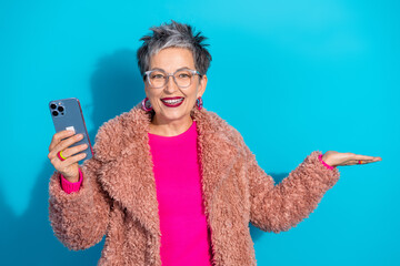Confident mature woman with grey hair wearing a pink sweater and furry coat promotes shopping on...
