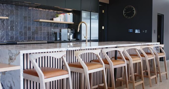 Camera is panning right across kitchen island revealing stools faucet and clock showing design