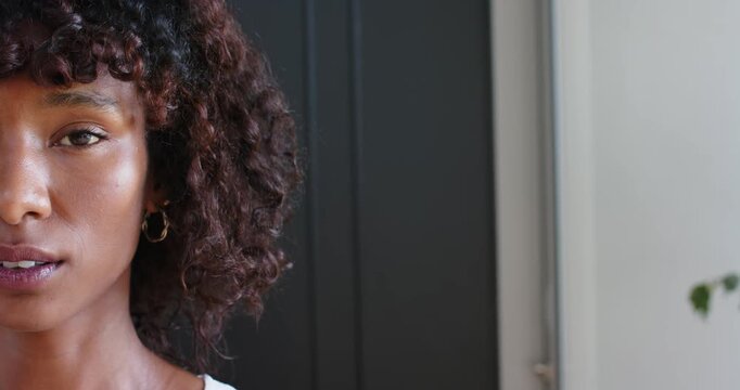 African American woman in 20s blinking, smiling, leaning forward at home with gold hoop, copy space