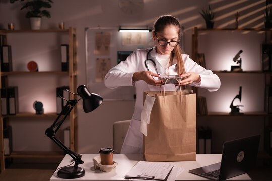 Consumption, medicine, healthcare and people concept. Woman doctor unpacking takeaway food in paper bag during night shift in the clinic.