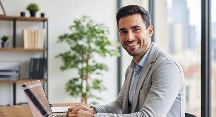 Fototapeta premium Confident Businessman Working on Laptop in Modern Office, Smiling at Camera