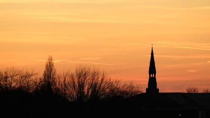 Dramatic sunset sky with vibrant orange clouds over a historic city silhouette.