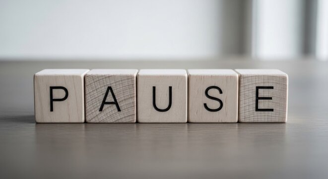 Wooden blocks spelling out "PAUSE" on a grey surface