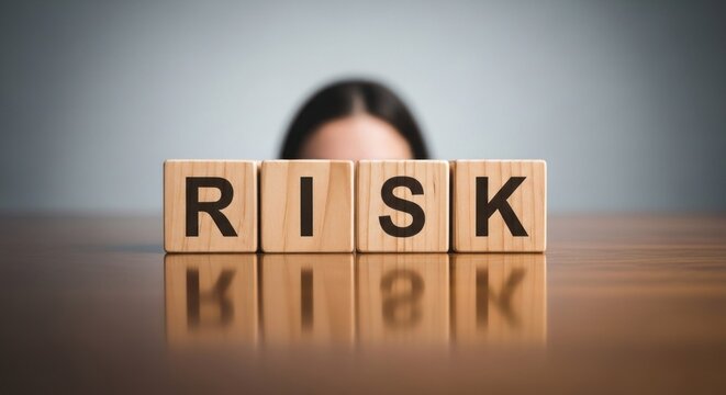 Wooden blocks spelling "RISK" are centered on a polished surface, a person's face partially visible