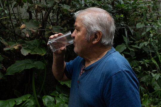 Hombre mayor bebiendo un vaso de agua fresca al aire libre en un jard&iacute;n.