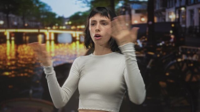 Young hispanic woman raises hands by illuminated canal on urban cobblestone street at night; uncertainty.