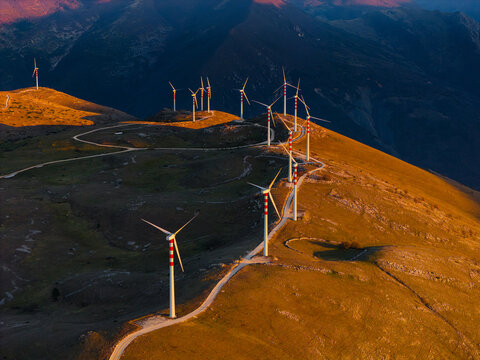 Aerial view of wind turbines standing tall against the backdrop of rugged mountains, bathed in the warm glow of the setting sun, Cocullo, Abruzzo, Italy.