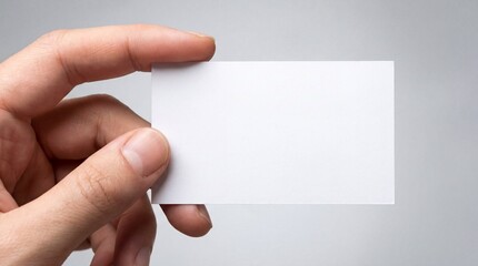 Obraz premium Close-up of a hand holding a blank white business card against a neutral background, minimal mockup template ideal for branding, identity design, corporate presentation, and contact information displa
