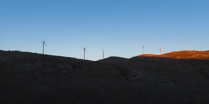 Aerial view of the golden sun kisses the tips of the wind turbines atop the dark, rugged hills, Cocullo, Abruzzo, Italy.