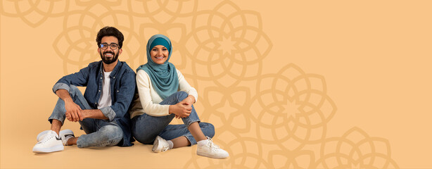 Two friends sit side by side on a light background. They wear casual clothes and smile while...