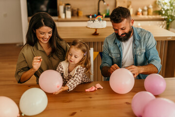 Family celebrating birthday with balloons and rainbow cake