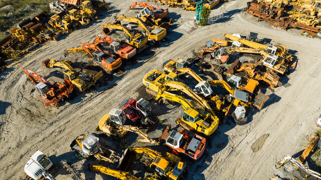 Aerial view of heavy construction equipment clustered in an open yard, a symphony of yellow, orange, and white machines against the neutral earth, Nanclares de la Oca, Basque Country, Spain.