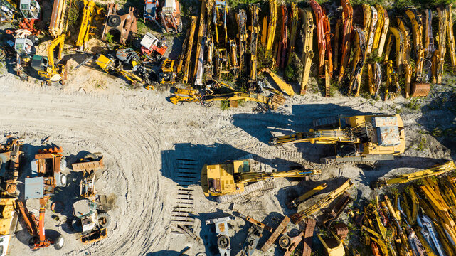 Aerial view of heavy machinery graveyard, rusting under the sun's glare, amidst muted earth tones and scattered debris, Nanclares de la Oca, Basque Country, Spain.