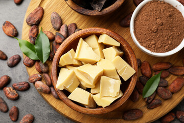 Fototapeta premium Organic cocoa butter, beans, powder and green leaves on grey table, top view