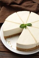 Tasty cut cheesecake with mint on wooden table, closeup