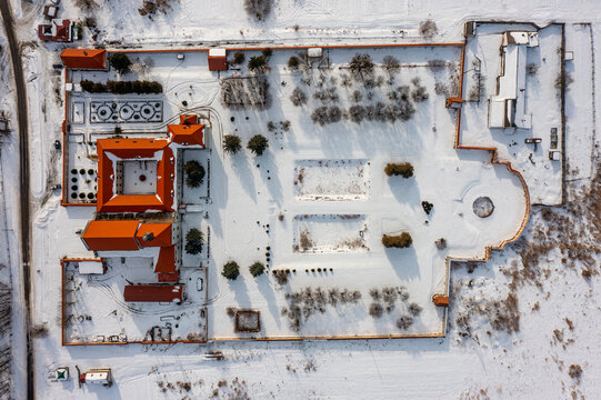 Aerial view of the snow-covered Olesko Castle's orange rooftops and walled courtyard stand out against the stark white landscape, Olesko, Lviv Oblast, Ukraine.
