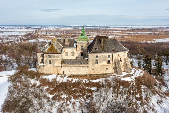 Aerial view of the imposing Olesko Castle, standing proudly on a snow-dusted hill against a backdrop of flat winter fields, Olesko, Lviv Oblast, Ukraine.