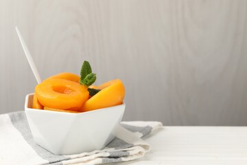 Pickled peaches and mint leaves in bowl on white wooden table, closeup. Space for text © New Africa
