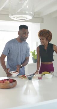 Vertical video: Couple placing bowl at kitchen island, arranging fruit and filming on phone tripod