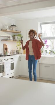 Vertical video: African American woman hearing music dancing singing headset with phone in kitchen