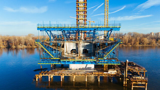 Aerial view of a colossal bridge pier under construction rises majestically from the water, its steel skeleton reflecting the clear sky, Novi Sad, Vojvodina, Serbia.