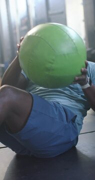 Vertical video: Male initiating core routine holding green medicine ball, twisting on gym floor