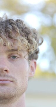 Vertical video: Man opening eyes after blink, meeting camera gaze outdoors with bokeh backlight