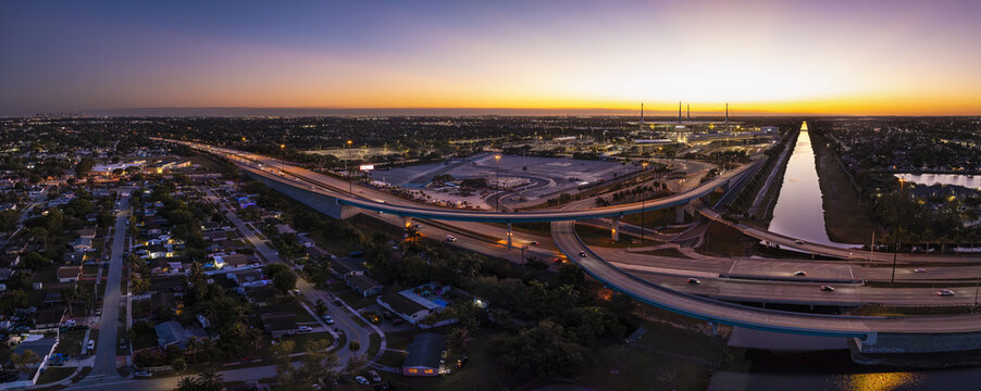 Aerial view of the Florida Turnpike interchange glowing with the warm hues of twilight, juxtaposed against the canal, Miami Gardens, Florida, United States.