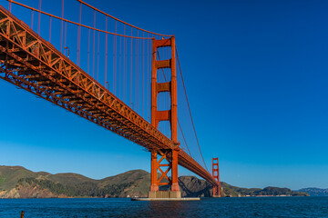 Fototapeta premium Golden Gate Bridge stands tall against a clear blue sky and calm water on a sunny day in San Francisco