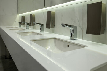 Modern Public Restroom Interior with White Marble Sinks and Automatic Chrome Faucets in Bathroom