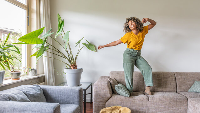 Happy afro american woman dancing on the sofa at home - Smiling girl enjoying day off lying on the couch - Healthy life style, good vibes people and new home concept