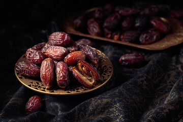 Dates fruits in a golden bowl on black fabric with gold ornamentation.