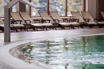Equipment in an indoor pool for back and neck massage in front of sun loungers. High-pressure water flow. Concept of relaxation, spa, and rejuvenation in a resort hotel. Tourism. © Юлия Клюева