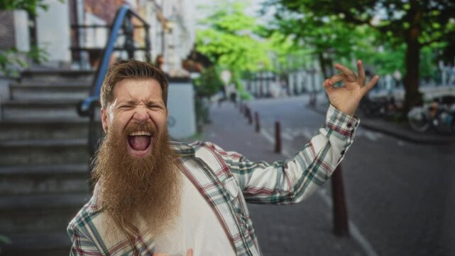 Young bearded man miming guitar playing with right hand strumming gesture on street; joyful creativity imagination.