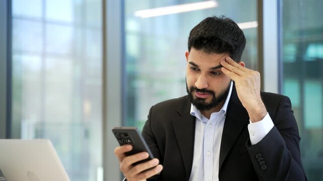 Worried businessman having problems with service or software on smartphone mobile phone sitting in business office. Stressed disappointed worker complains about bad internet connection. Close up