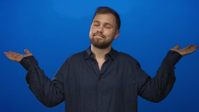 Young caucasian man shrugging with raised hands in studio wearing dark shirt and slight smirk; casual indifference.