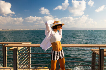 Slender woman stands on the embankment and looks at the ocean. Summer vacation by the sea. Freedom and relaxation on the seashore.