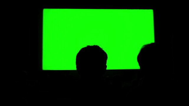 People Silhouettes Sitting in Movie Theater Facing Green Screen