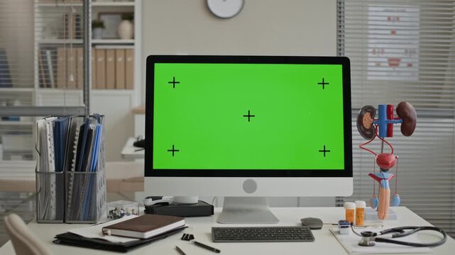 Indoor eye level no people shot of desktop computer with green screen and tracking markers on desk in modern medical office, kidney anatomy model and medical supplies visible
