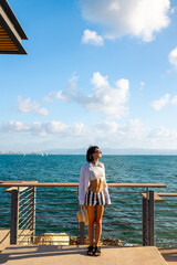 Sensual girl with piercing and sunglasses poses in the sun with dark hair fluttering in the wind. Calm brunette stands against golden evening sunset.