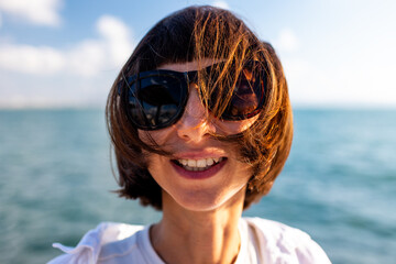 portrait of attractive woman, smiling, brunette, confident, pretty standing near the sea. Girl smiles and looks at camera.