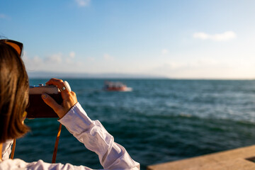 girl taking picture of ship standing on embankment. Beautiful female tourist enjoying sea view while relaxing on weekend. girl using camera.
