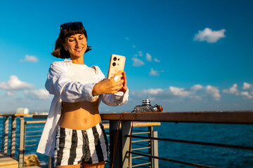 Attractive smiling tourist taking a selfie on her mobile phone against the backdrop of the Mediterranean Sea. The girl enjoys her vacation and shoots content for social media.