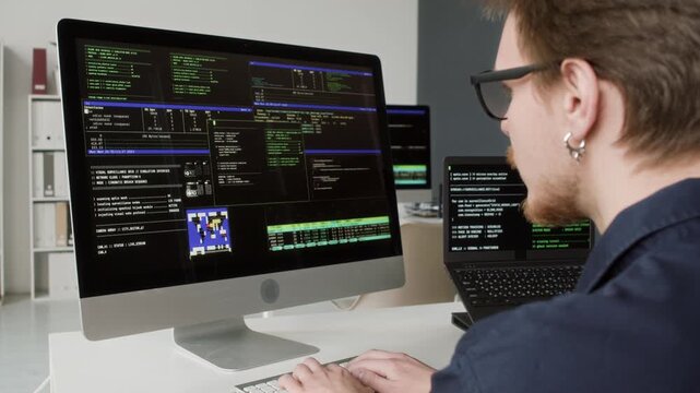 Over shoulder shot of young adult male computer programmer with glasses typing on keyboard debugging system or application errors while working at office desk