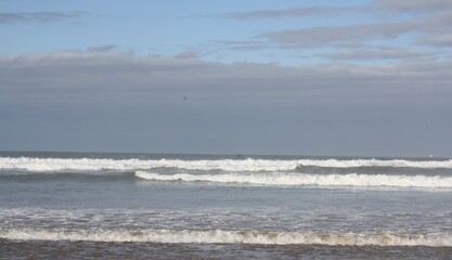 Obraz premium Agadir beach on the Atlantic coast with blue waves and golden sand, Agadir Oufella rising on the hill in the distance under bright sunlight, scenic panoramic view. Photo taken Feb 18, 2026.
