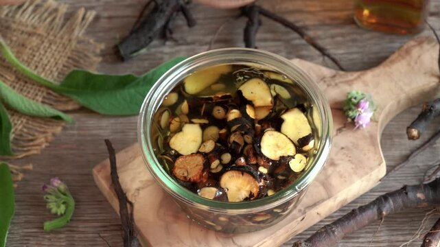 Pouring sliced comfrey or knitbone root into a jar containing alcohol - preparation of homemade herbal tincture