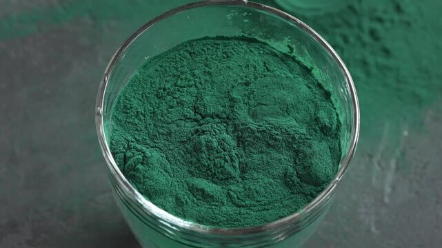 Pouring green spirulina algae powder into a glass of water. Nutritional supplement.