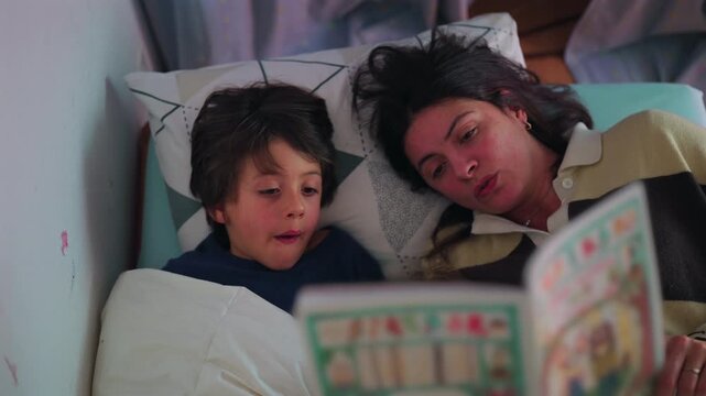 Mother reading bedtime story to young son who is yawning in bed, tender family moment showing sleepiness comfort and evening routine at home