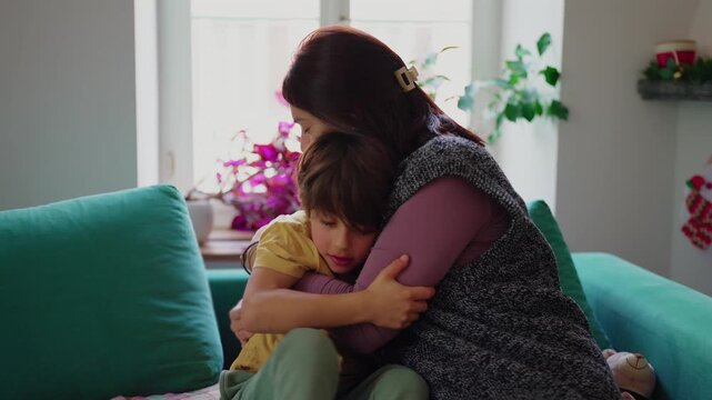 Mother hugging young son on couch, tender family moment of comfort reassurance and emotional support in bright living room at home