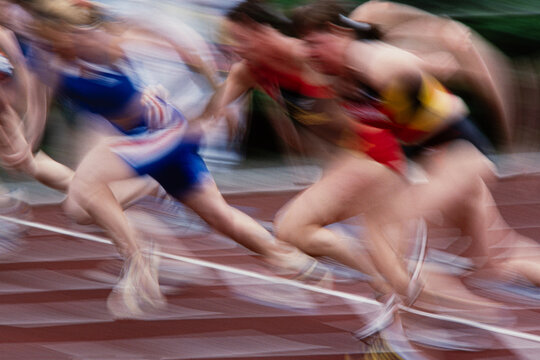 Explosive motion blur of sprinters launching off starting blocks, high-speed sprint start in track and field competition. Vintage 35mm film scan.